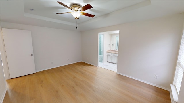 empty room featuring a tray ceiling, ceiling fan, and light hardwood / wood-style flooring