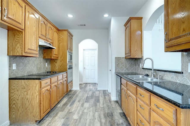 kitchen with tasteful backsplash, dark stone countertops, sink, and light hardwood / wood-style flooring