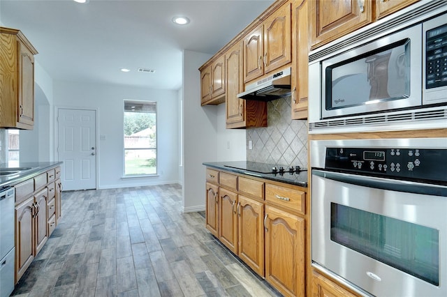 kitchen with decorative backsplash, appliances with stainless steel finishes, sink, wood-type flooring, and dark stone countertops