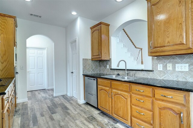 kitchen with sink, stainless steel dishwasher, backsplash, dark stone counters, and wood-type flooring