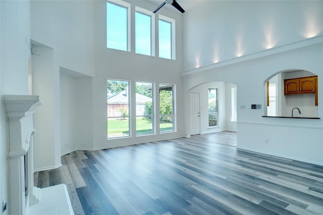 unfurnished living room with hardwood / wood-style flooring, ceiling fan, and a towering ceiling