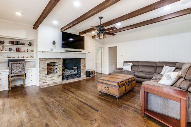 living room featuring ceiling fan, beam ceiling, dark hardwood / wood-style flooring, and a brick fireplace