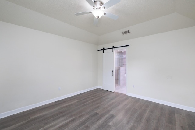 unfurnished room with dark wood-type flooring, ceiling fan, a barn door, and vaulted ceiling