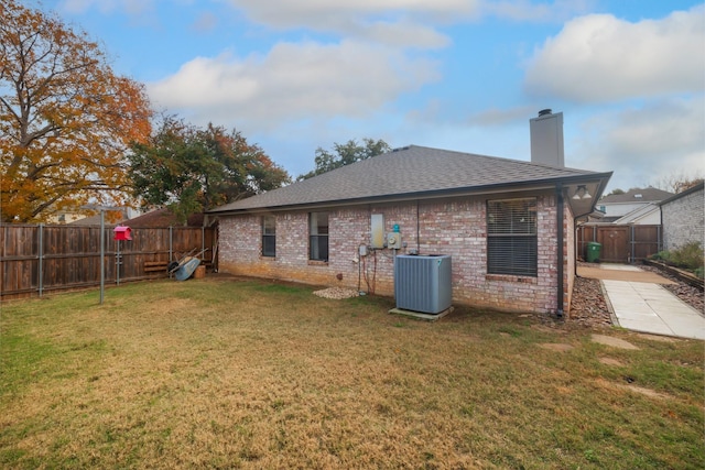 rear view of property featuring central AC unit and a lawn