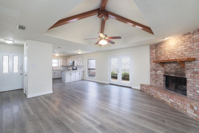 unfurnished living room with french doors, vaulted ceiling with beams, a textured ceiling, a fireplace, and hardwood / wood-style floors