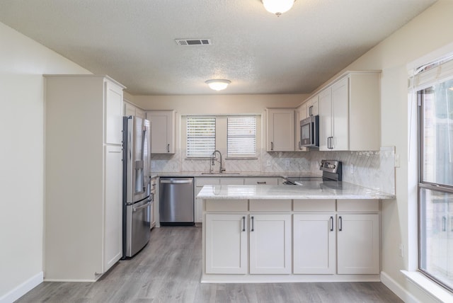 kitchen with sink, kitchen peninsula, white cabinets, stainless steel appliances, and backsplash