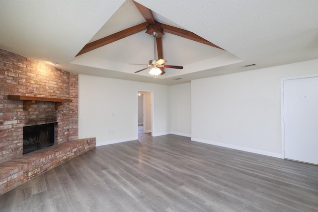 unfurnished living room featuring dark wood-type flooring, vaulted ceiling with beams, a fireplace, and a tray ceiling