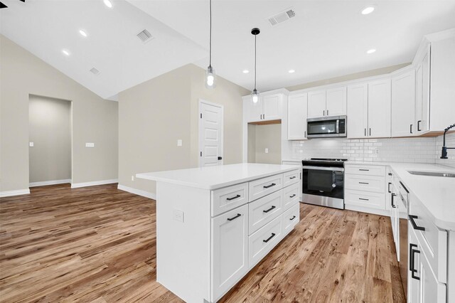 kitchen featuring sink, white cabinetry, stainless steel appliances, a kitchen island, and decorative light fixtures