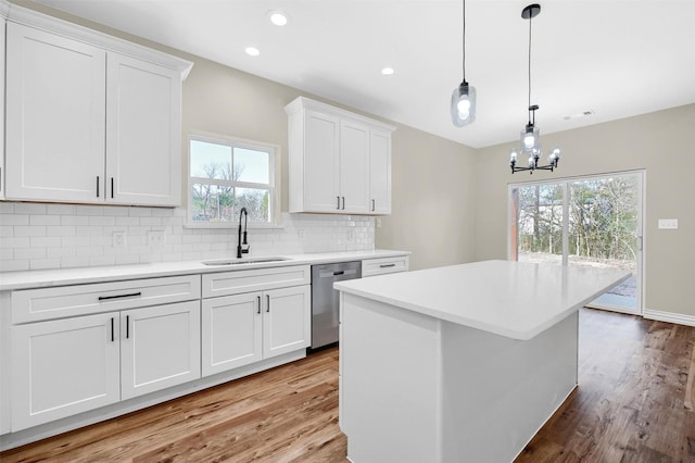 kitchen featuring sink, white cabinetry, decorative light fixtures, stainless steel dishwasher, and a kitchen island