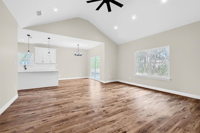 unfurnished living room with ceiling fan with notable chandelier, sink, hardwood / wood-style floors, and high vaulted ceiling