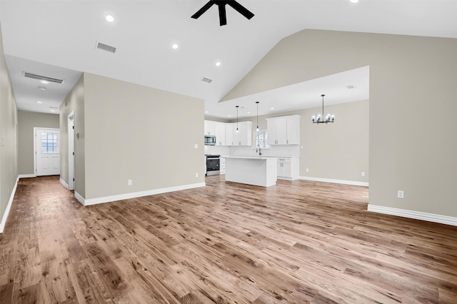 unfurnished living room with high vaulted ceiling, sink, ceiling fan with notable chandelier, and light wood-type flooring