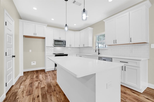 kitchen featuring sink, a center island, appliances with stainless steel finishes, pendant lighting, and white cabinets