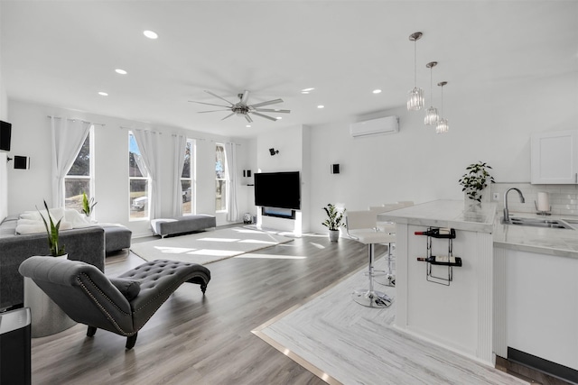 living room with ceiling fan, sink, a wall unit AC, and light hardwood / wood-style floors