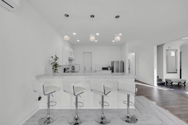 kitchen featuring decorative light fixtures, white cabinetry, kitchen peninsula, stainless steel appliances, and a wall unit AC