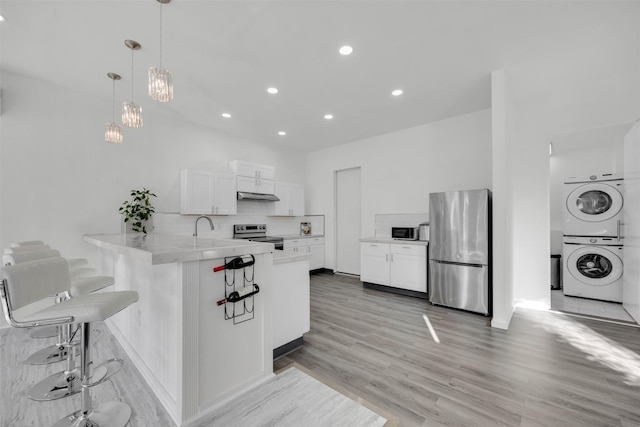 kitchen featuring decorative light fixtures, white cabinets, stacked washer / drying machine, kitchen peninsula, and stainless steel appliances