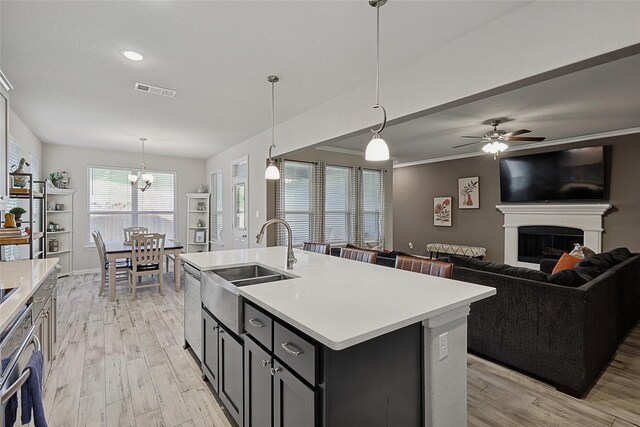 kitchen featuring a kitchen island with sink, hanging light fixtures, ceiling fan with notable chandelier, and light hardwood / wood-style floors