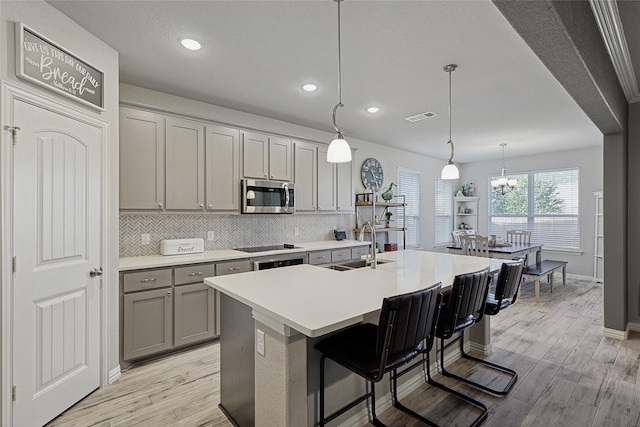 kitchen featuring pendant lighting, backsplash, a center island with sink, light wood-type flooring, and a breakfast bar area