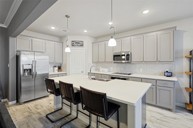 kitchen with light wood-type flooring, tasteful backsplash, stainless steel appliances, sink, and hanging light fixtures