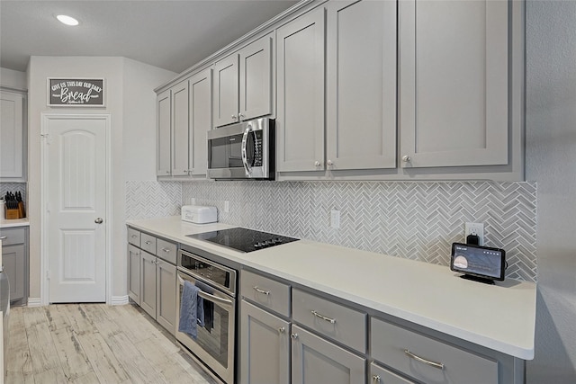 kitchen featuring light wood-type flooring, stainless steel appliances, gray cabinets, and tasteful backsplash