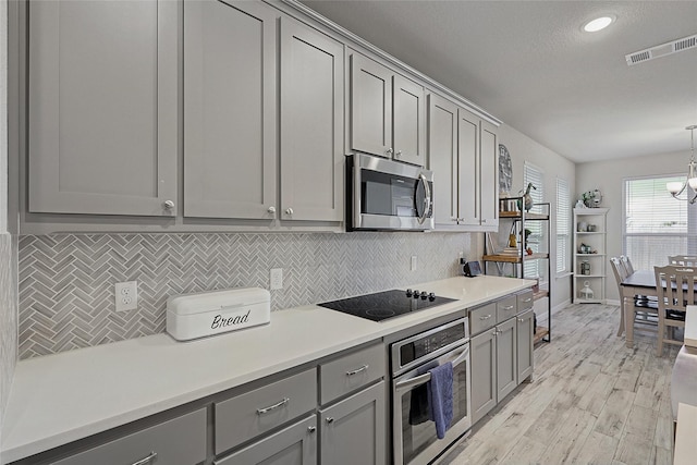 kitchen featuring gray cabinetry, light hardwood / wood-style flooring, decorative light fixtures, and appliances with stainless steel finishes