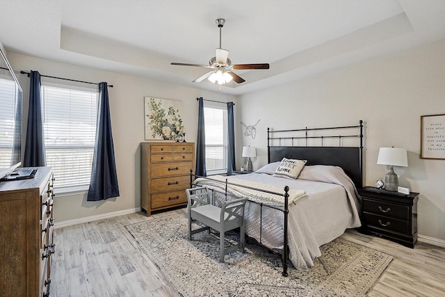 bedroom featuring ceiling fan, a tray ceiling, and light hardwood / wood-style flooring