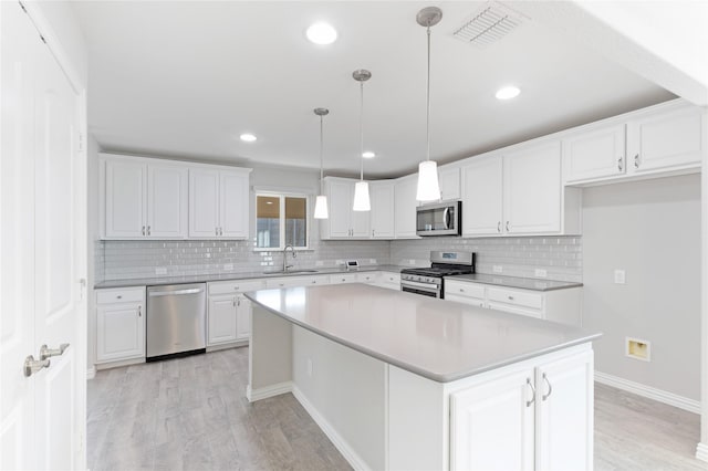 kitchen with pendant lighting, sink, appliances with stainless steel finishes, a center island, and white cabinets