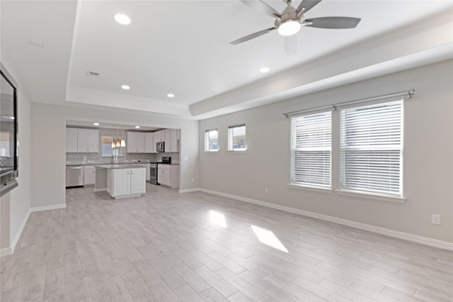 unfurnished living room with light hardwood / wood-style floors, a raised ceiling, and ceiling fan