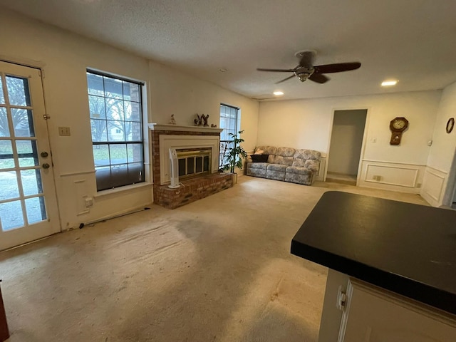 unfurnished living room featuring ceiling fan, light colored carpet, a textured ceiling, and a brick fireplace