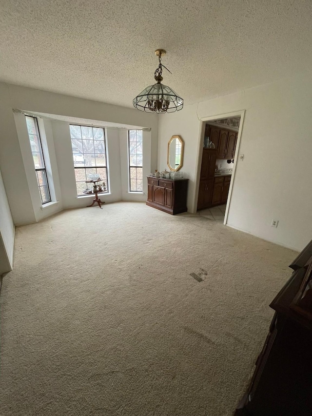 spare room featuring a chandelier, light carpet, and a textured ceiling