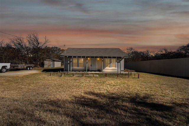 back house at dusk with a porch and a lawn