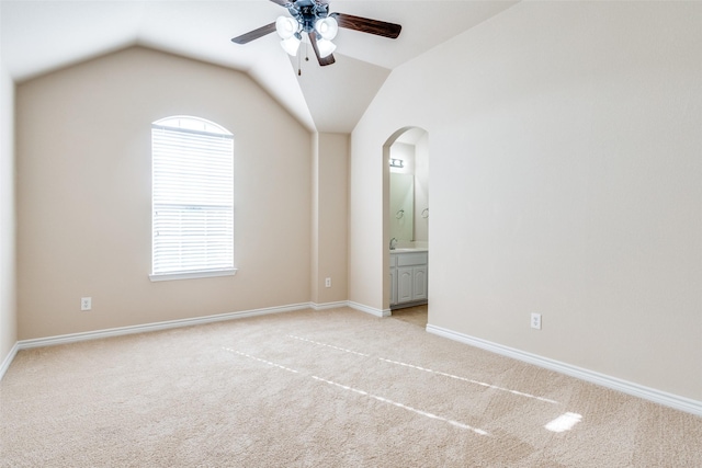 unfurnished bedroom featuring ensuite bathroom, lofted ceiling, light colored carpet, and ceiling fan