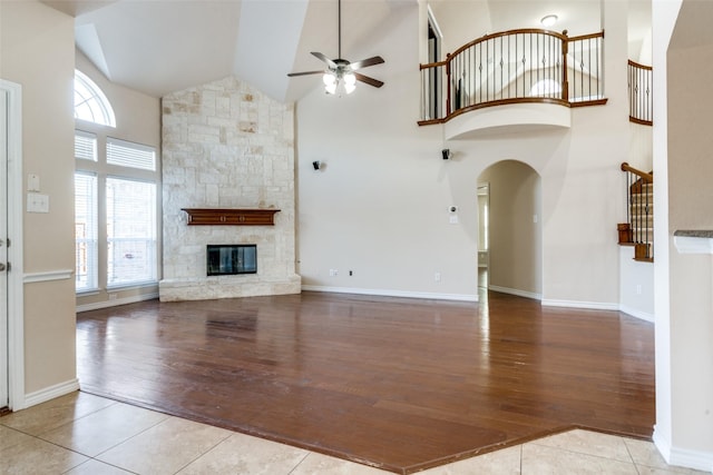 unfurnished living room with a stone fireplace, light hardwood / wood-style flooring, high vaulted ceiling, and ceiling fan