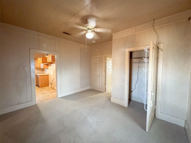 unfurnished bedroom with wood walls, ensuite bath, light colored carpet, a closet, and ceiling fan