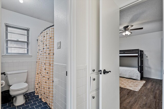 bathroom with a textured ceiling, hardwood / wood-style floors, tile walls, toilet, and ceiling fan