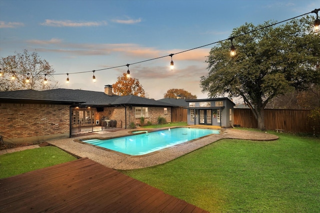 pool at dusk featuring a wooden deck, a lawn, and an outdoor structure