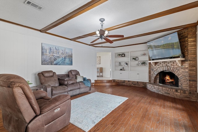 living room featuring a textured ceiling, a brick fireplace, built in shelves, beam ceiling, and ceiling fan