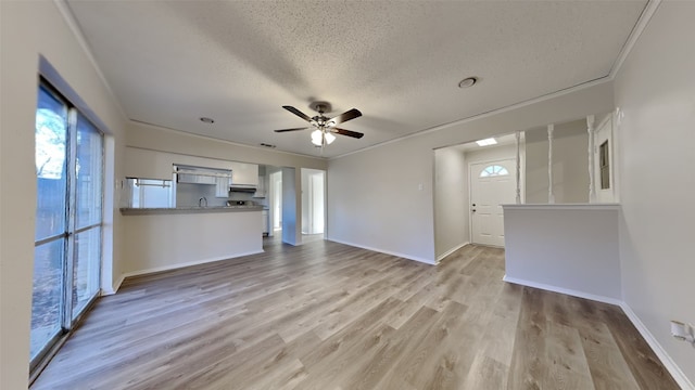 unfurnished living room featuring a textured ceiling, light wood-type flooring, ceiling fan, and ornamental molding