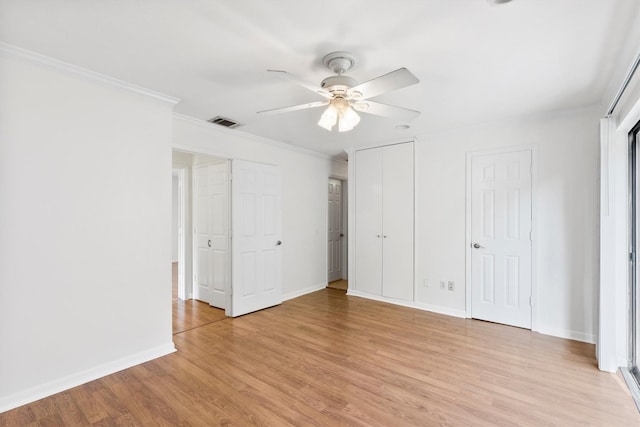 unfurnished bedroom featuring ceiling fan, light wood-type flooring, crown molding, and two closets