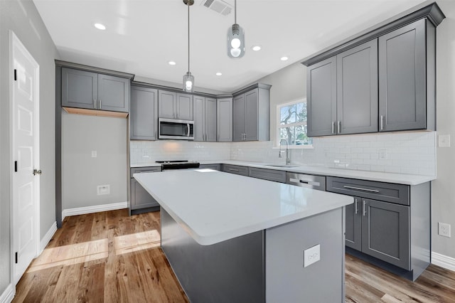 kitchen with sink, gray cabinetry, hanging light fixtures, a kitchen island, and stainless steel appliances