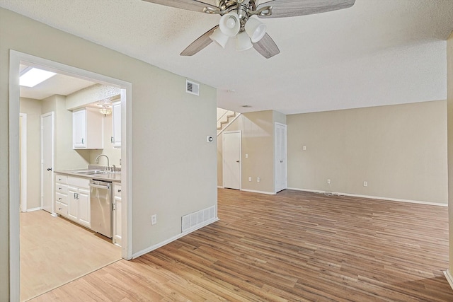 unfurnished living room with ceiling fan, sink, a textured ceiling, and light wood-type flooring