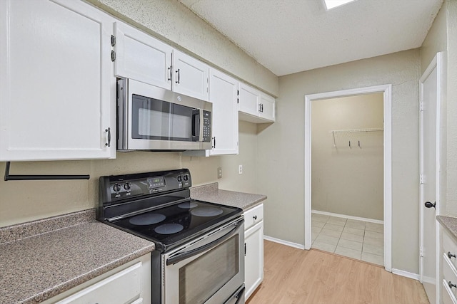 kitchen with electric range, light hardwood / wood-style floors, white cabinetry, and a textured ceiling