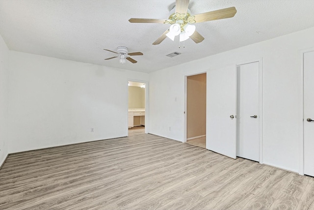 unfurnished bedroom with a textured ceiling, light wood-type flooring, ensuite bath, and ceiling fan