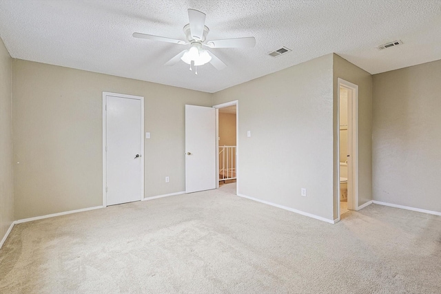 unfurnished bedroom with ensuite bath, ceiling fan, a textured ceiling, light colored carpet, and a closet