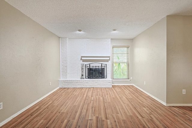 unfurnished living room with a brick fireplace, a textured ceiling, and light wood-type flooring