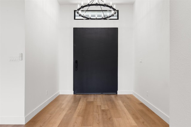 foyer featuring light wood finished floors, an inviting chandelier, and baseboards