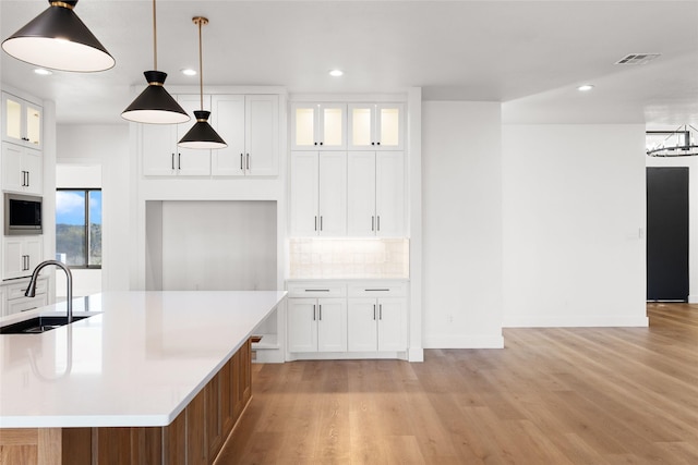 kitchen with stainless steel microwave, visible vents, decorative backsplash, a sink, and light wood-type flooring