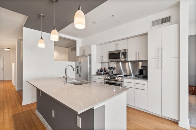 kitchen with white cabinetry, sink, hanging light fixtures, appliances with stainless steel finishes, and light wood-type flooring