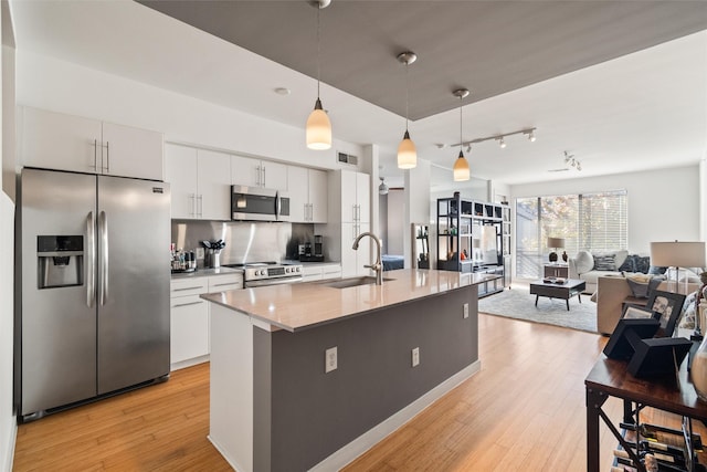 kitchen featuring a center island with sink, appliances with stainless steel finishes, sink, white cabinetry, and decorative light fixtures