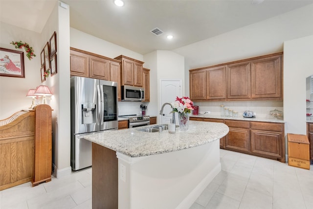 kitchen with sink, appliances with stainless steel finishes, light stone countertops, a center island with sink, and decorative backsplash