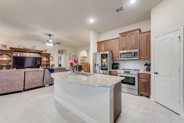 kitchen featuring sink, light stone counters, tasteful backsplash, appliances with stainless steel finishes, and a kitchen island with sink